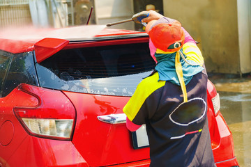 Car wash service., Self-cleaning car wash., The young man was washing the car to be clean and safe from germs., The young man is spraying the water on the roof of the car for cleanliness.