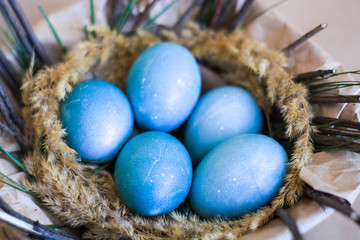 Easter holiday, background and decor of painted blue eggs in nest of flowers, branches. Religion and traditions.