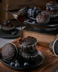 chocolate vegan muffins on a wooden background. Blueberry  on side. Dark and moody photo style.