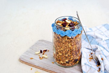 Homemade baked oat granola with nuts, dried cranberries and honey in a glass jar on a light...