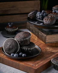 chocolate vegan muffins on a wooden background. Blueberry  on side. Dark and moody photo style.