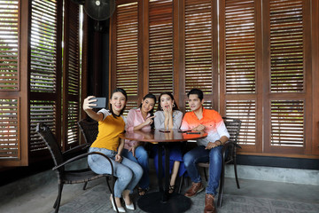 Group young asian malay man woman at rustic wooden cafe table meet talk discuss business study selfie self portrait hand smart phone