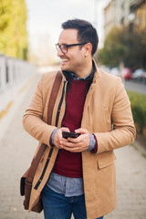 Businessman with eyeglasses standing on the street holding phone.