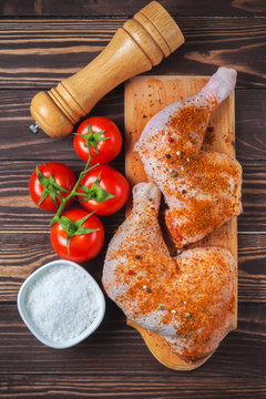Raw chicken legs on a cutting board on a wooden table. Marinated chicken leg with spices and tomatoes. Vertical photo