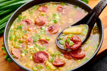 Dry Pea Soup with meat sausages, potato, green onions and sesame. Yellow Pea Soup in black bowl at dark slate background.