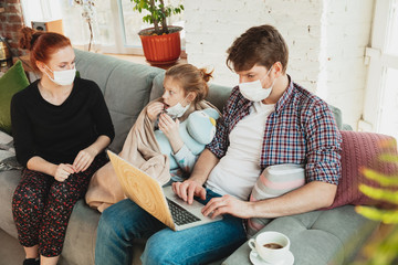 Caucasian famiy in face masks and gloves isolated at home with coronavirus respiratory symptoms such as fever, headache, cough in mild condition. Healthcare, medicine, quarantine, treatment concept.