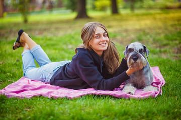 Fototapeta premium Pretty girl with his Schnauzer dog at nature park outdoor is standing and posing in front of camera. Portrait of owner and Rough collie dog enjoys, resting and petting together on city street.