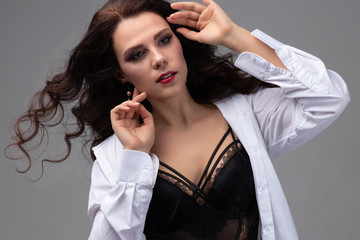Fototapeta premium Attractive girl posing is studio on grey background. Brunette fashion beauty model with long curly hair that waving in the wind. Concept of face care or hairstyling in salon