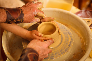 A close-up of the hand of a male potter who teaches his pupil, a child of the art of making a pot or a vase of clay. People working on potters.