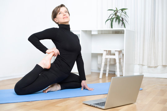 Young woman doing yoga exercises online on a laptop. Fitness at home in video chat.
