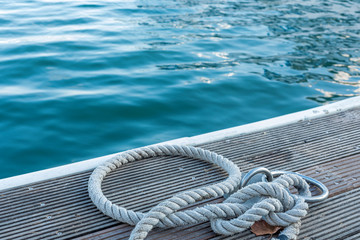 Mooring cable on the pier. Сloseup of wooden cleats with nautical moored ropes, blue sea. Copy...