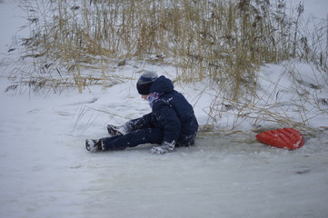 The boy sat in a puddle rolling on the ice