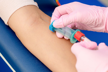 Nurse takes blood sampling introducing a needle into a vein of woman's arm.