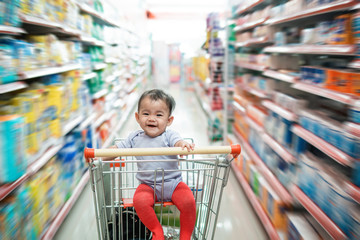 happy infant baby sitting alone in shopping cart or trolley in grocery supermarket