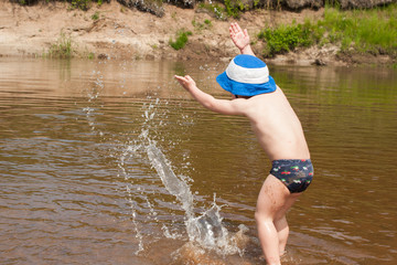 Cute baby boy splashes on the riverbank