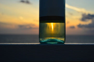 The bottle of white wine with sunset in reflection and on the background