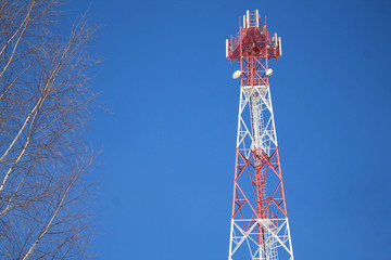 Cell tower of red and white color against a blue sky.