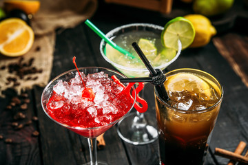 Fresh sweet alcohol cocktails in different glasses, long island cosmopolitan and margarita on the dark wooden background, closeup, horizontal