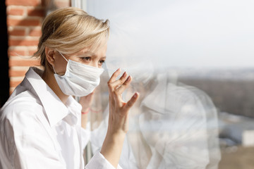 Illness girl on home quarantine. Girl in protective medical masks sits on windowsill and looks out window. Virus protection, coronavirus pandemic, prevention epidemic.