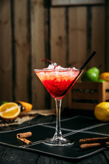 Fresh sweet red cosmopolitan cocktail in glass with crushed ice on the dark wooden background, side view