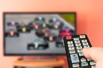  Caucasian man watching formula 1 race on TV at home. Changing channels and adjusting volume with television remote control.  © cronislaw