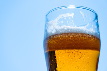 Light beer in a glass goblet on a background of blue sky. Beer foam on the walls of a glass in the sunlight.