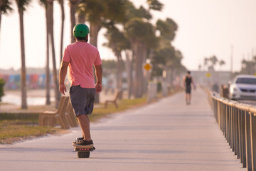 Man rides on electric onewheel skateboard or unicycle. Outdoor fun activities. Sun on a seafront promenade.