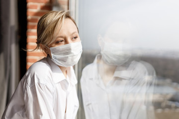 Illness girl on home quarantine. Girl in protective medical masks sits on windowsill and looks out window. Virus protection, coronavirus pandemic, prevention epidemic.