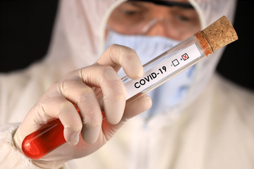 The doctor in a protective suit and mask holding a glass tube with a positive blood test result for...