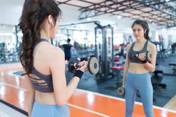 Fototapeta na wymiar Asian woman lifting dumbbells in fitness room. Young woman lifting dumbbells in the gym.
