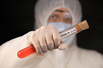 The doctor in a protective suit and mask holding a glass tube with a positive blood test result for...