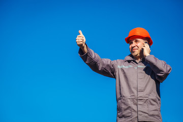 Construction worker in a helmet against the blue sky talking on the phone. Contractor control...