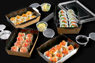 Conceptual photo for sushi roll delivery. Rolls in cardboard packages on a black background. 3 types of spicy rolls with salmon, scallop and tuna, rolls with salmon and onions