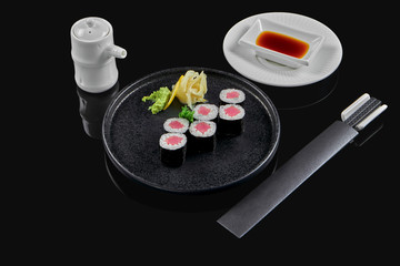 Obraz na płótnie Canvas Traditional maki sushi rolls with tuna on a black plate in composition with soy sauce and chopsticks on a black background. Japanese food. Photo for the menu