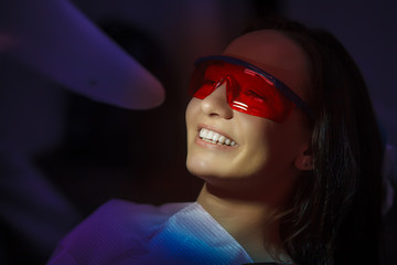 Close-up portrait of a female patient at dentist in the clinic. Teeth whitening procedure with ultraviolet light UV lamp.