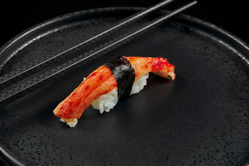 Classic sushi with crab and rice on a black ceramic plate with black stylish chopsticks. Traditional japanese food. Photo for the menu