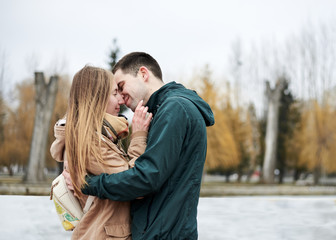 Fototapeta premium Young couple in love, wearing beige and green casual jackets, standing in front of frozen lake hugging, kissing each other in winter. Valentines day romantic celebration outside