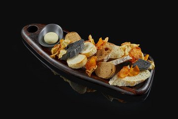 Different types of bread - white, rye and ink cuttlefish on a wooden tray on a black background. Bread plate in a restaurant