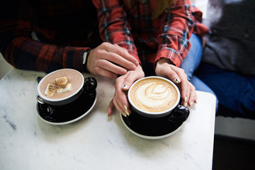 Two mugs of coffee on the table. Man's and women's hands are holding cups with cappuccino and hot chocolate with marshmallow..Romantic Valentines day celebration. Couple on a cafe date.