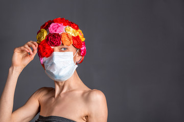 Woman with medical mask wearing artificial flower hat isolated over grey background. copy space