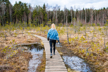 Girl hiking on a wooden path in Trakai historical national park, botanical zoological reserve, cognitive trail, long winding path over the bog in the forest, swamp, marsh, tiny lakes