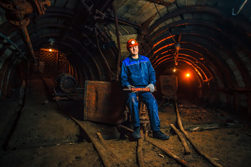 A miner in a coal mine stands near a trolley. Copy space.