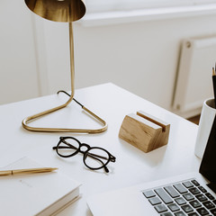 Minimalist workspace with laptop, notebook, lamp, glasses on white table. Working study....