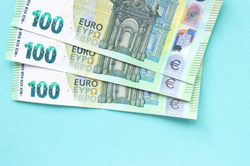 Three banknotes in denominations of 100 euros. They lie on top of each other in the form of a fan on a blue background. Money and finance concept