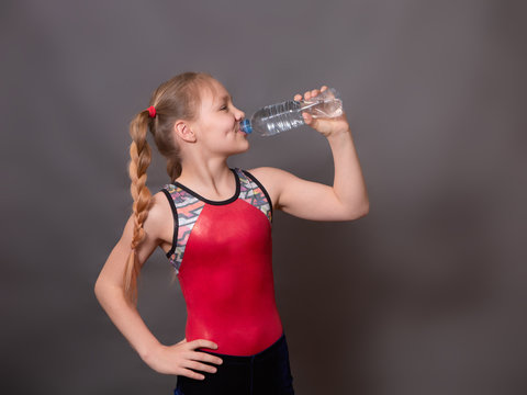 
A Girl Athlete In A Red Sports Swimsuit Smiles And Drinks Water From A Bottle
