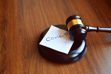 Judges gavel or law mallet and word covid-19 on sound block on dark brown wooden texture...