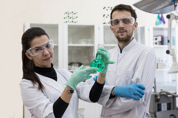 Obraz premium Two chemists work in a modern chemical laboratory. Senior chemist and laboratory assistant study the green solution in the flask.