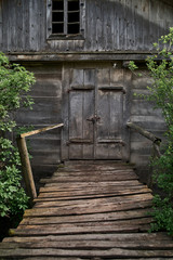 Old wooden grey hut in the village. Old time watermill among green trees in countryside. Doors of ancient wooden building,