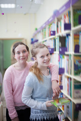  girls of 13 years old choosing   book in   library.