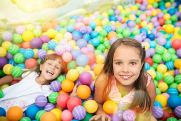 Two girls playing in pool with colorful plastic balls in game room. Child looking at camera